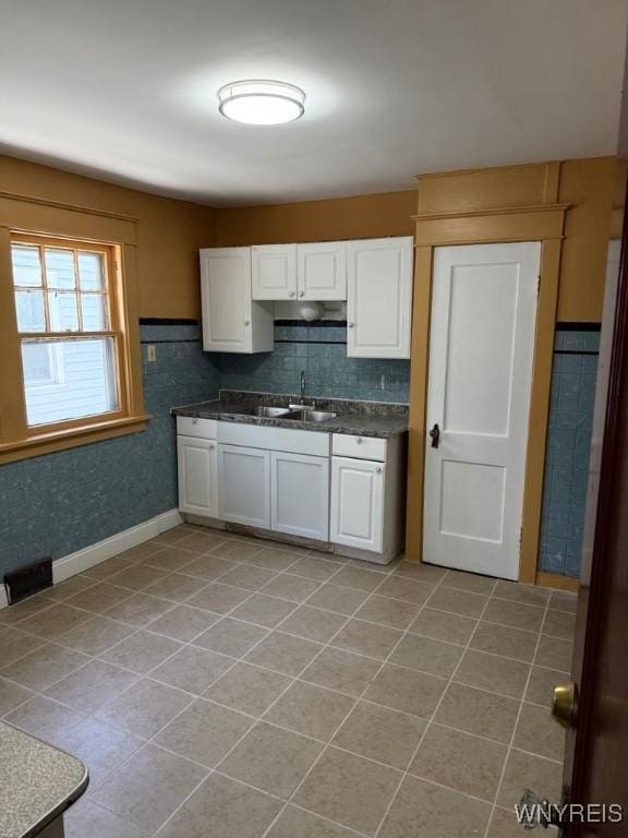 kitchen featuring dark countertops, light tile patterned flooring, white cabinetry, and a sink