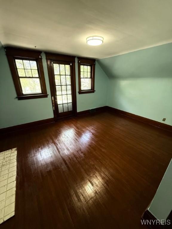 additional living space featuring dark wood finished floors, baseboards, and vaulted ceiling
