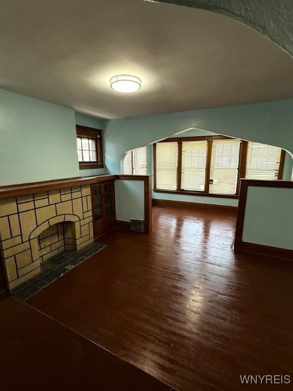 unfurnished living room with wood finished floors, a stone fireplace, and baseboards