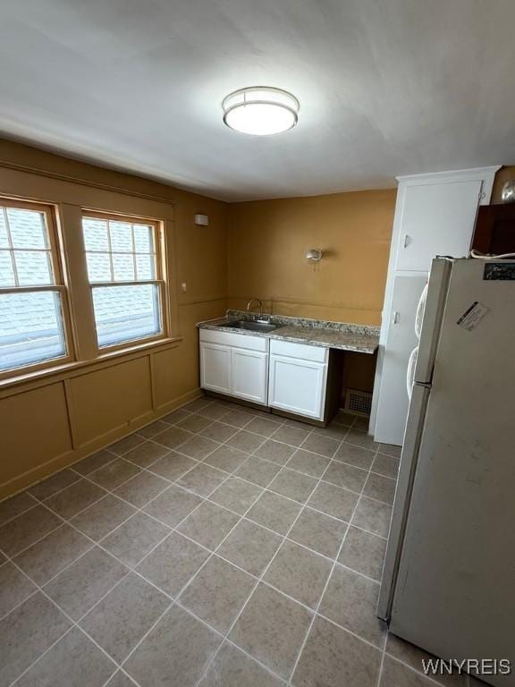 kitchen with freestanding refrigerator, a sink, light tile patterned floors, and white cabinetry