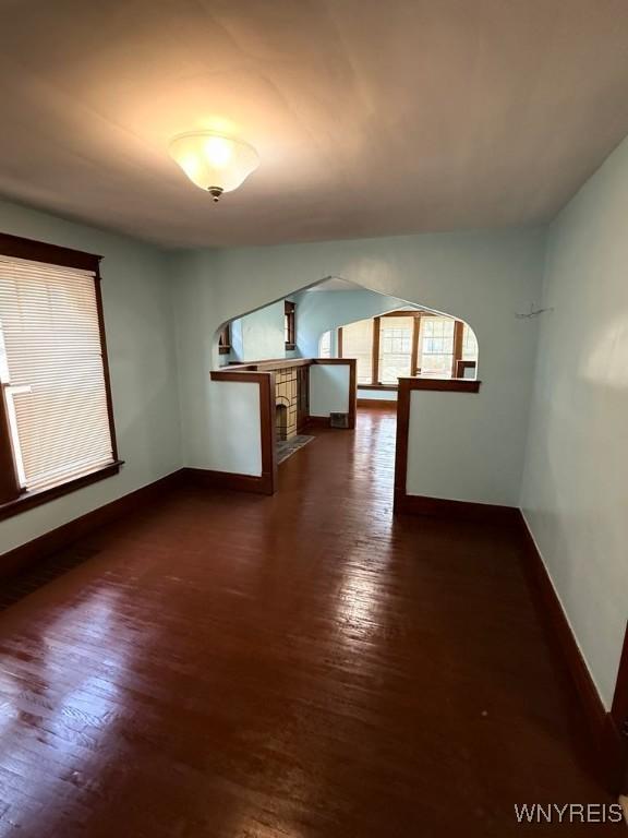 unfurnished living room with baseboards, dark wood-style floors, arched walkways, and a fireplace