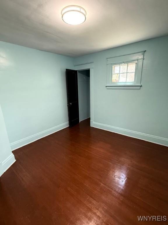unfurnished bedroom featuring baseboards, wood finished floors, and a closet