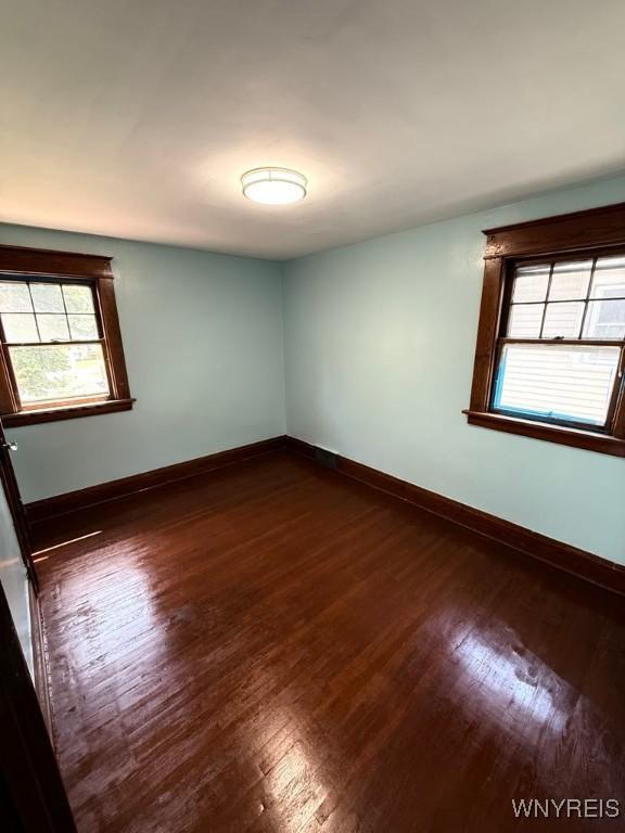 empty room featuring dark wood-style flooring, plenty of natural light, and baseboards