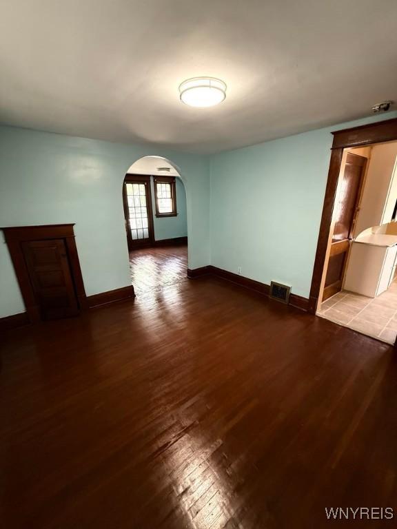 unfurnished room featuring arched walkways, hardwood / wood-style flooring, and baseboards