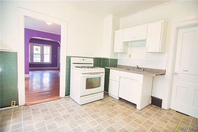 587 Goodyear Ave, Buffalo, NY 14211 - kitchen featuring white gas range oven, white cabinetry, arched walkways, a sink, and baseboards