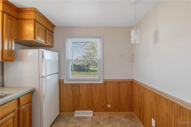 103 Pulaski St, Syracuse, NY 13204 - kitchen with a wainscoted wall, wooden walls, freestanding refrigerator, brown cabinets, and decorative light fixtures
