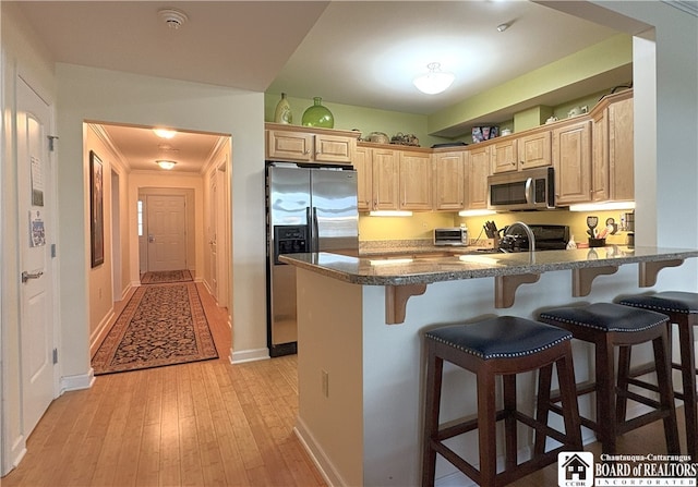 50 Lakeside Dr Unit C103, Ellery, NY 14712 - kitchen featuring appliances with stainless steel finishes, a peninsula, light brown cabinetry, light wood-type flooring, and a breakfast bar