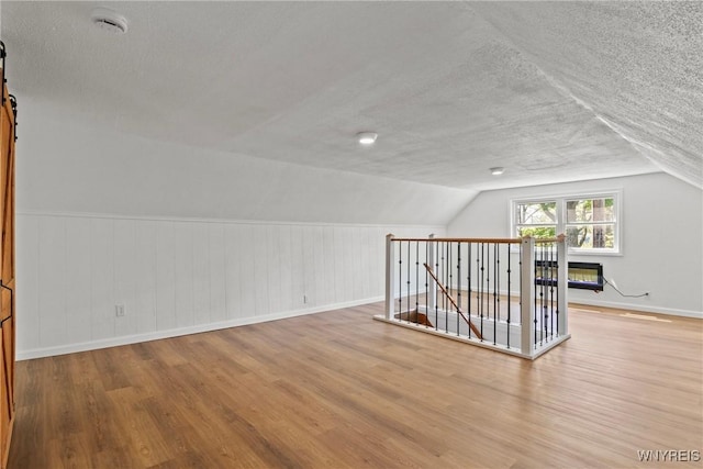 5302 William St, Lancaster, NY 14086 - additional living space with a textured ceiling, wood finished floors, baseboards, lofted ceiling, and a barn door