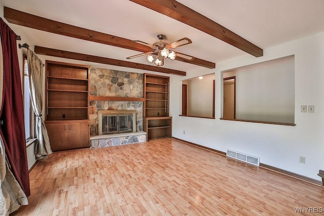 2227 W River Rd, Grand Island, NY 14072 - unfurnished living room featuring wood finished floors, baseboards, a ceiling fan, a stone fireplace, and beam ceiling