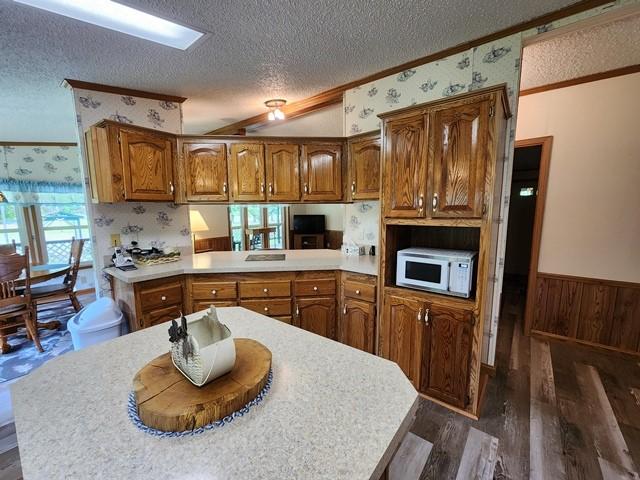 3483 First Fork Rd, Grove Twp, PA 15861 - kitchen featuring white microwave, a textured ceiling, ornamental molding, brown cabinetry, and wainscoting