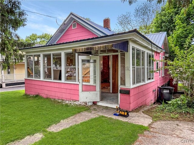 102 Milton Ave, Syracuse, NY 13204 - view of front of home featuring a sunroom, a chimney, a front lawn, and metal roof