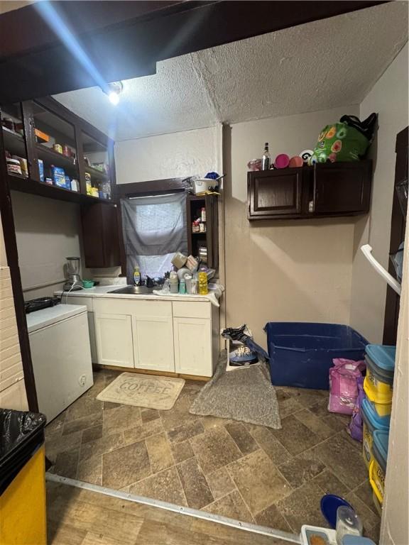 213 Flint St, Rochester, NY 14608 - kitchen featuring stone finish flooring, white cabinetry, a sink, a textured ceiling, and refrigerator