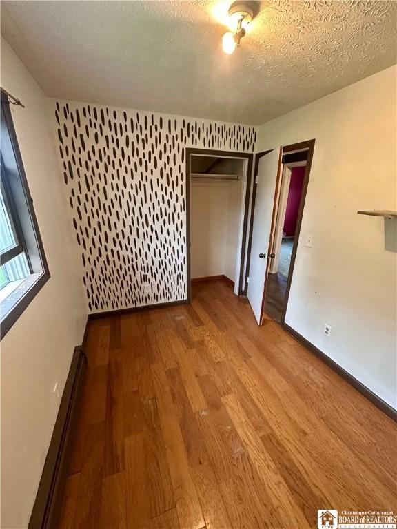 538 Erie St, Olean-City, NY 14760 - unfurnished bedroom featuring wood finished floors, baseboard heating, a closet, baseboards, and a textured ceiling