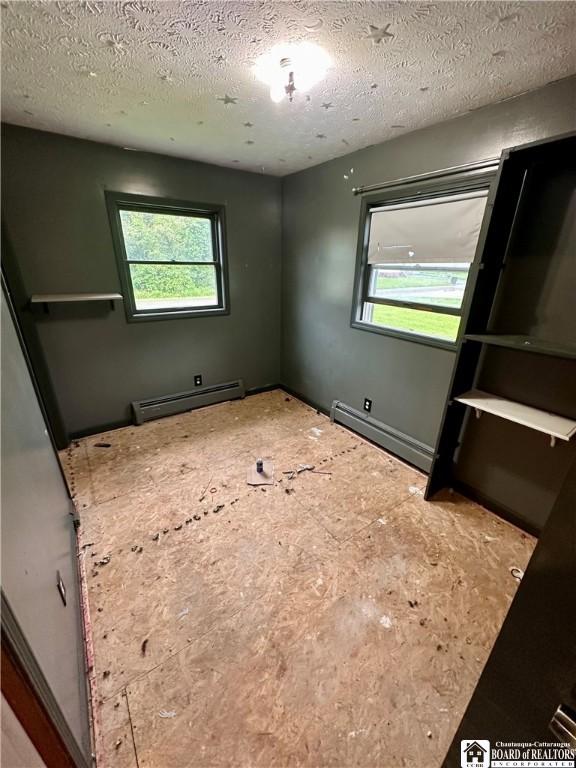 538 Erie St, Olean-City, NY 14760 - unfurnished bedroom featuring a baseboard heating unit, baseboard heating, multiple windows, and a textured ceiling