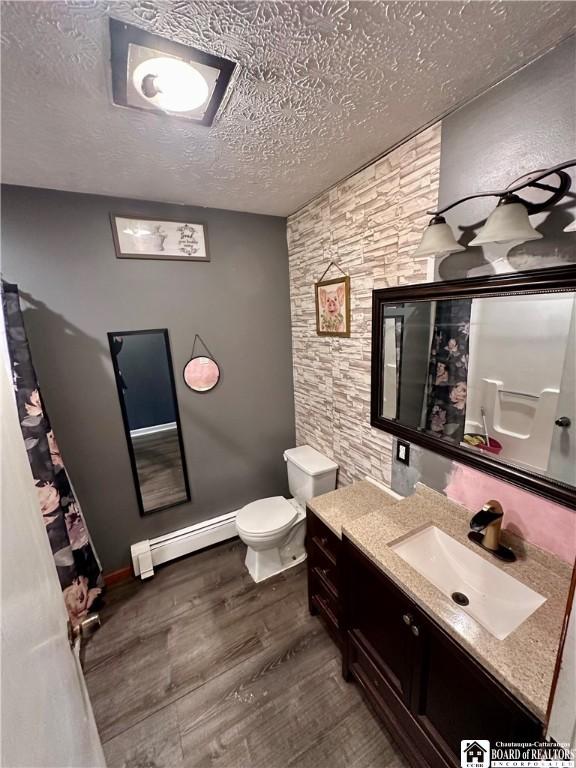 538 Erie St, Olean-City, NY 14760 - full bathroom featuring baseboard heating, toilet, a textured ceiling, vanity, and wood finished floors