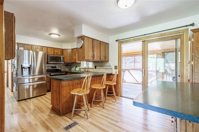 7425 Eelpot Rd, Naples, NY 14512 - kitchen featuring stainless steel appliances, dark countertops, a peninsula, brown cabinetry, and light wood finished floors