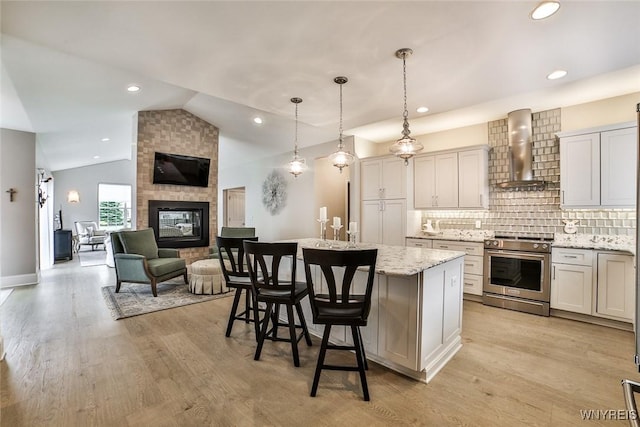 5692 Ferncrest Ct Unit B, Clarence, NY 14032 - kitchen with stainless steel electric range, wall chimney exhaust hood, vaulted ceiling, a center island with sink, and a multi sided fireplace