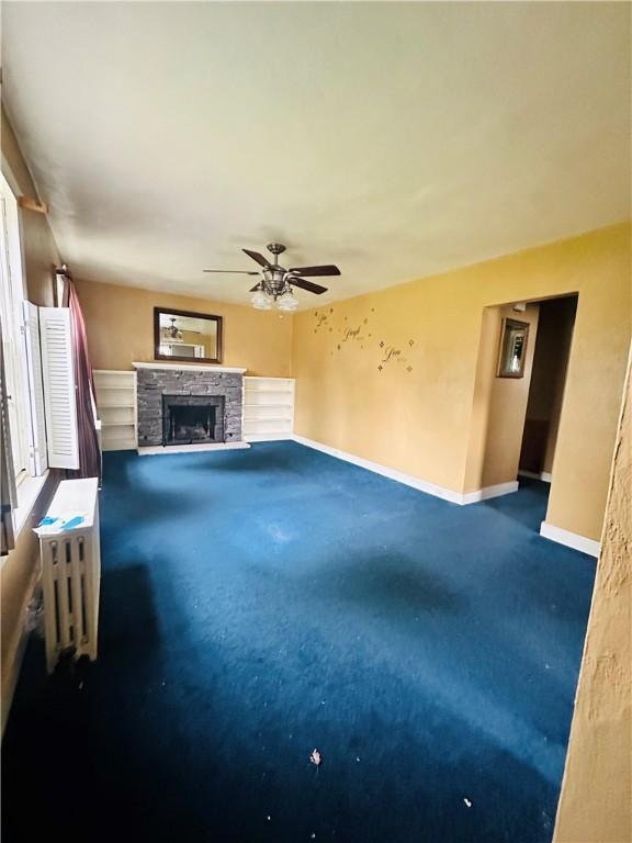 218 Grant St, Elmira-City, NY 14901 - unfurnished living room featuring carpet, a stone fireplace, baseboards, and ceiling fan