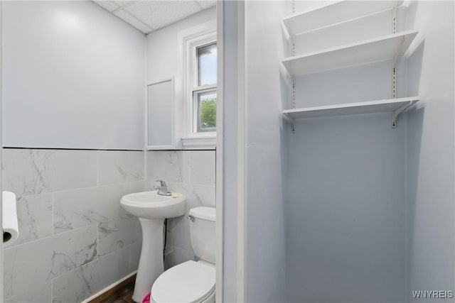 2452 Niagara Ave, Niagara Falls, NY 14305 - bathroom featuring toilet, tile walls, a paneled ceiling, and wainscoting