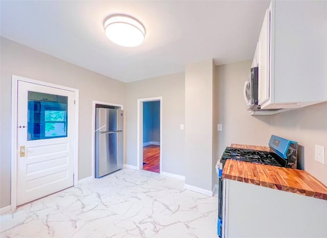 561 Post St, Elmira-City, NY 14904 - kitchen with stainless steel appliances, wooden counters, light marble finish floors, white cabinetry, and baseboards