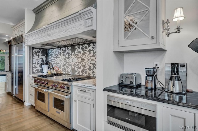 1225 W Arnold Dr, Hamburg, NY 14085 - kitchen featuring built in appliances, premium range hood, dark stone counters, light wood-type flooring, and white cabinetry