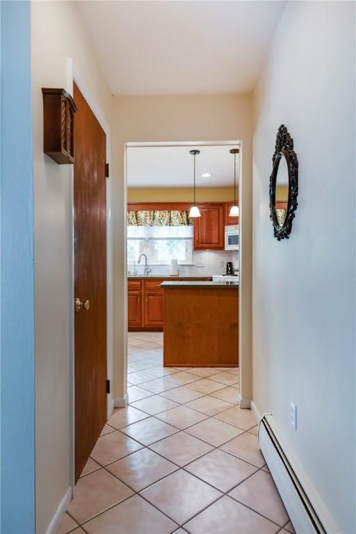 61 Brookside Cir, Big Flats, NY 14903 - kitchen featuring a baseboard radiator, white microwave, brown cabinets, a sink, and light tile patterned floors
