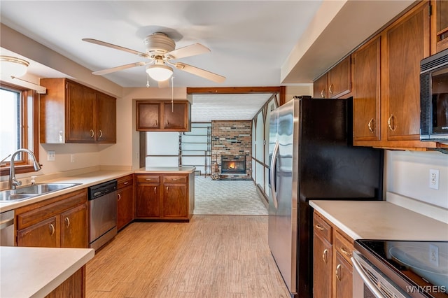 7415 Colonial Dr, Niagara, NY 14305 - kitchen with stainless steel appliances, a sink, a brick fireplace, brown cabinetry, and light wood-style flooring