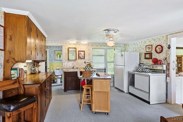 7078 Fuller Rd, Aurelius, NY 13140 - kitchen featuring wallpapered walls, stove, a kitchen island, freestanding refrigerator, and a breakfast bar area