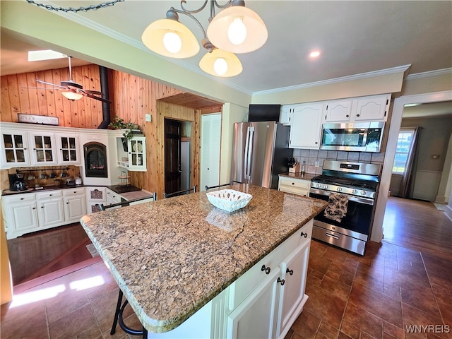 3666 S Hill Rd, Hamburg, NY 14075 - kitchen featuring stainless steel appliances, ornamental molding, wooden walls, white cabinetry, and tasteful backsplash