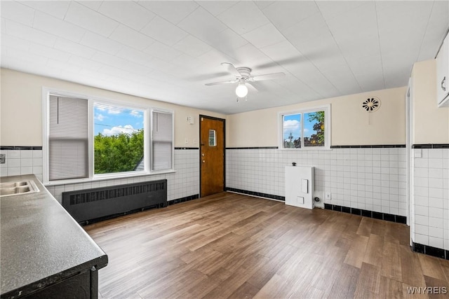 2365 Genesee St, Cheektowaga, NY 14225 - kitchen with radiator heating unit, wood finished floors, a ceiling fan, a sink, and tile walls