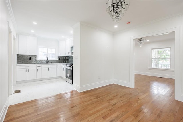 636 Ridge Rd, Webster, NY 14580 - kitchen featuring stainless steel range with gas stovetop, a chandelier, crown molding, white cabinets, and tasteful backsplash