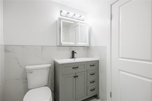 636 Ridge Rd, Webster, NY 14580 - bathroom with marble finish flooring, toilet, vanity, tile walls, and a wainscoted wall