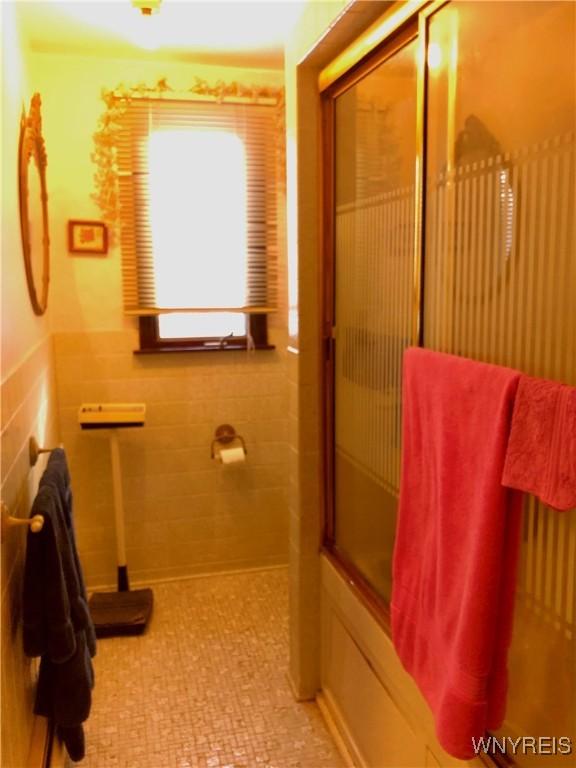 148 Marlin Rd, Grand Island, NY 14072 - bathroom with bath / shower combo with glass door, a wainscoted wall, and tile walls