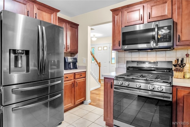 4343 Lockport Rd, Cambria, NY 14094 - kitchen featuring appliances with stainless steel finishes, light countertops, light tile patterned floors, backsplash, and brown cabinets