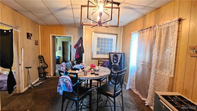 55 Lewis St, Buffalo, NY 14206 - dining room featuring wood walls, a drop ceiling, a chandelier, dark colored carpet, and baseboards