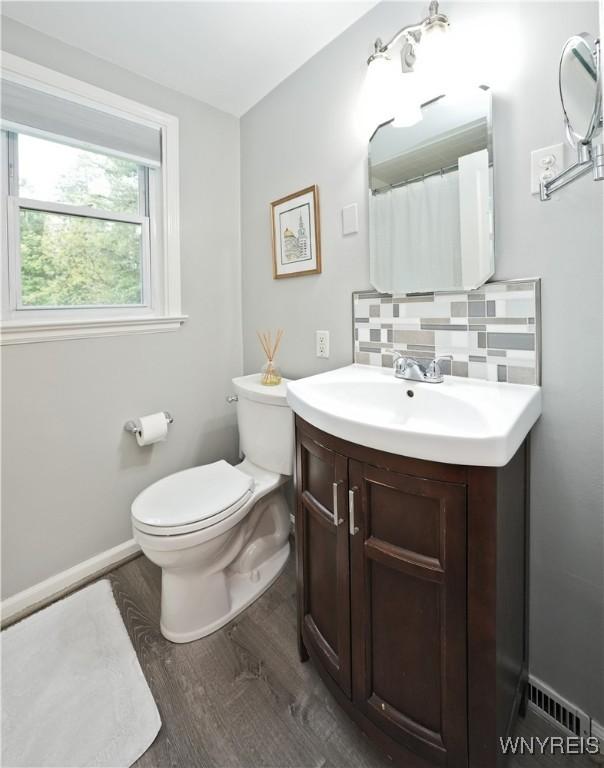 4334 Connection Dr, Clarence, NY 14221 - full bath with wood finished floors, toilet, vanity, decorative backsplash, and baseboards