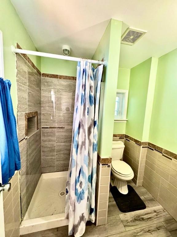 450 Stover Rd, Tyrone, NY 14815 - full bath with tile walls, toilet, a stall shower, wainscoting, and wood finished floors