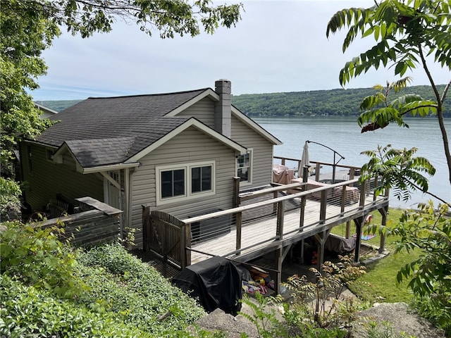 8976 Trio Dr, Urbana, NY 14840 - rear view of house featuring a deck with water view, a chimney, and roof with shingles
