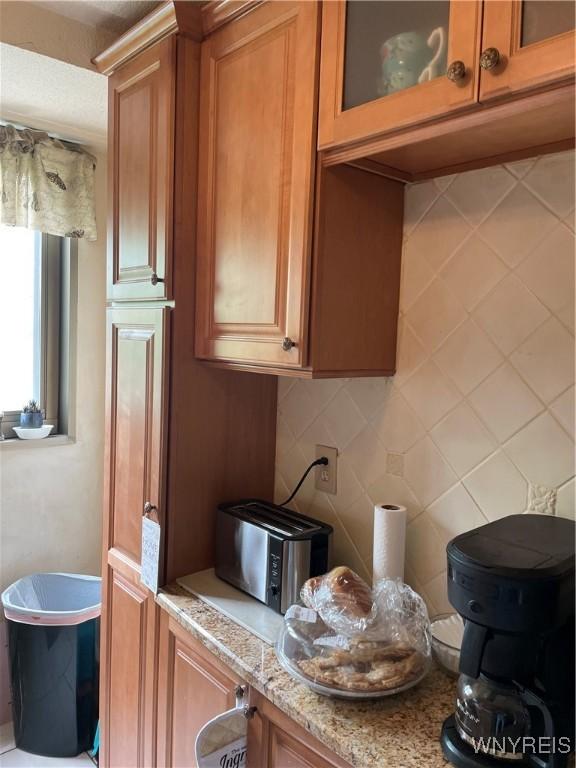 151 Buffalo Ave Unit 404, Niagara Falls, NY 14303 - kitchen featuring brown cabinets, glass insert cabinets, light stone countertops, and tasteful backsplash