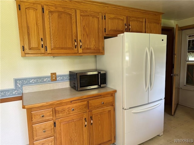 725 Warren Dr, Aurora, NY 14052 - kitchen with freestanding refrigerator, stainless steel microwave, wallpapered walls, brown cabinetry, and light countertops
