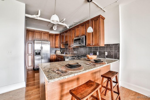 132 Lakefront Blvd Unit 204, Buffalo, NY 14202 - kitchen with stainless steel appliances, light stone countertops, baseboards, a peninsula, and light wood-style floors