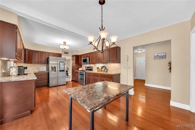 8918 Hurlburt Ln, Clarence, NY 14031 - kitchen featuring appliances with stainless steel finishes, tasteful backsplash, a chandelier, wood-type flooring, and baseboards