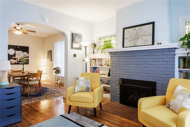 43 Woodland Park, Rochester, NY 14610 - living room featuring arched walkways, a ceiling fan, a brick fireplace, ornamental molding, and wood finished floors
