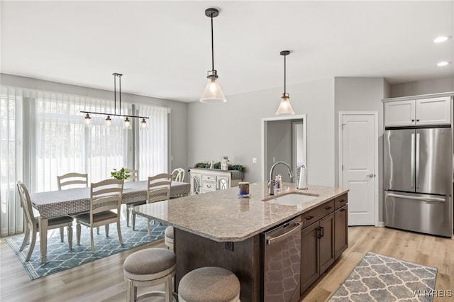 1167 Guinevere Dr, Greece, NY 14626 - kitchen with stainless steel appliances, a sink, light wood finished floors, light stone countertops, and a center island with sink