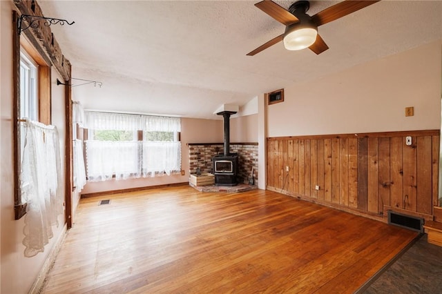 6695 Fisher Rd, Ontario, NY 14589 - unfurnished living room featuring a wood stove, wood finished floors, ceiling fan, and a wainscoted wall
