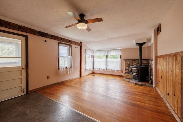 6695 Fisher Rd, Ontario, NY 14589 - unfurnished living room with a wood stove, a textured ceiling, a ceiling fan, wood finished floors, and baseboards