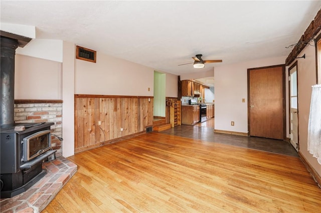 6695 Fisher Rd, Ontario, NY 14589 - unfurnished living room featuring a wood stove, light wood-style floors, ceiling fan, wainscoting, and baseboards
