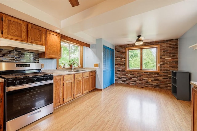 6695 Fisher Rd, Ontario, NY 14589 - kitchen featuring stainless steel gas stove, under cabinet range hood, a ceiling fan, a sink, and brick wall