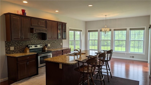 12 Probst Rd, Mendon, NY 14534 - kitchen with stainless steel range with electric cooktop, light stone countertops, decorative backsplash, a breakfast bar area, and a kitchen island with sink