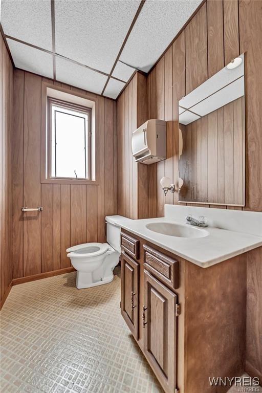 3045 Niagara St, Niagara Falls, NY 14303 - half bathroom with vanity, toilet, wood walls, and a paneled ceiling